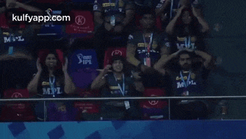 a group of people are sitting in a stadium with their hands on their heads .