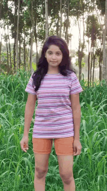 a girl in a striped shirt and shorts is standing in the grass