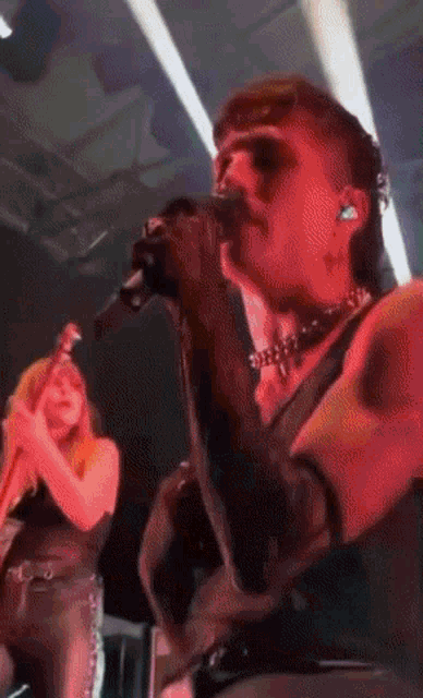 a man is singing into a microphone while a woman plays a guitar in the background