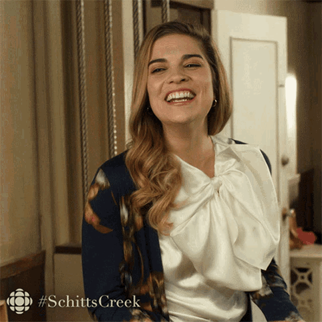 a woman is laughing with a #schittscreek logo in the corner