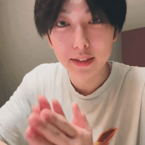a young man wearing a white t-shirt is clapping his hands together