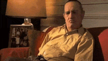 a man in a yellow shirt sits on a couch in front of a picture of a family