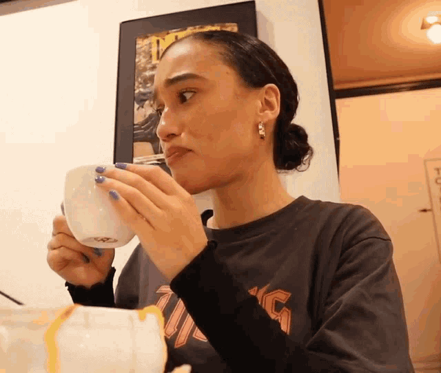 a woman wearing a black shirt with the letter g on it is drinking from a white cup