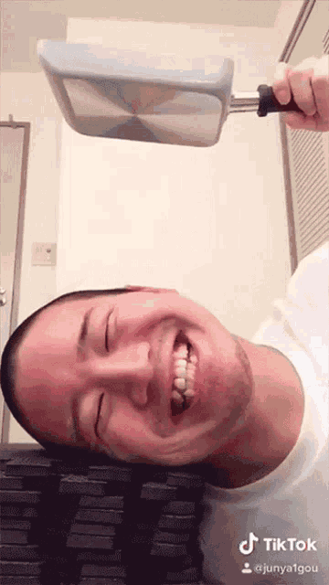 a man is smiling while holding a frying pan in front of his face and the words tiktok are on the bottom