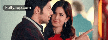 a man and a woman are looking at each other and the woman is pointing at the man 's face .