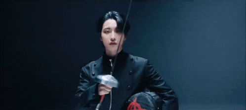 a young man in a black jacket is holding a sword and a helmet .
