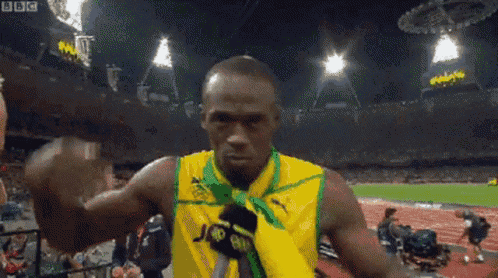 a man in a yellow shirt with a medal around his neck is talking into a microphone .