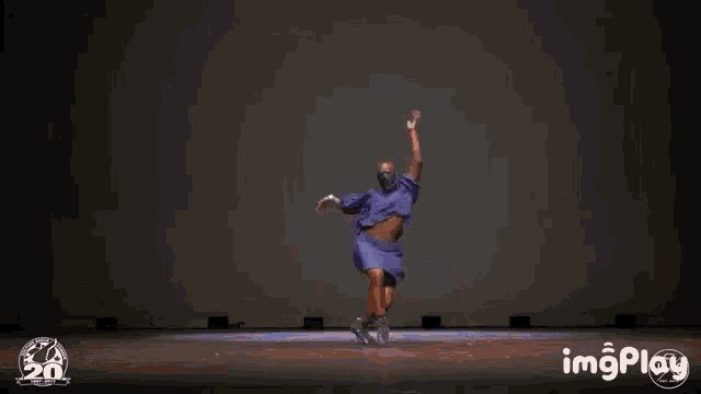a man in a purple dress is dancing on a stage with the words imgplay behind him