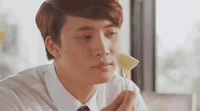 a man in a white shirt and tie is eating a piece of fruit on a toothpick