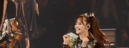 a woman with a crown on her head is smiling and dancing on stage