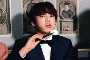 a man in a tuxedo and bow tie is holding a brush in his mouth .