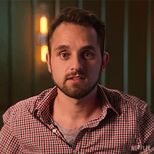 a man with a beard wearing a plaid shirt is looking at the camera .