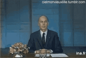 a man in a suit and tie sitting at a desk with the words au revoir