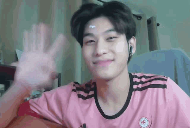 a young man wearing a pink adidas shirt waves