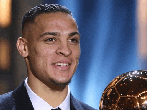 a man in a suit and tie is holding a soccer ball and smiling