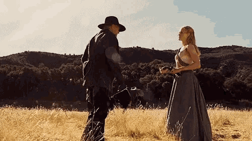 a man and a woman are standing in a field holding hands .