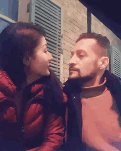a man and woman are kissing in front of a brick wall