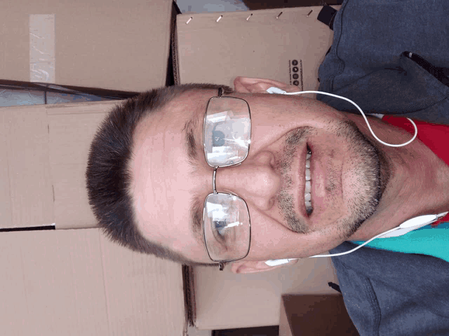 a man wearing glasses and ear buds stands in front of a cardboard box that says ' boo ' on it