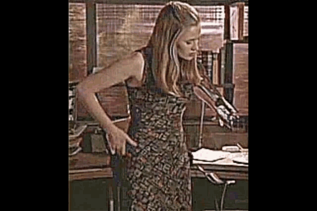 a woman in a dress is standing in front of a desk in an office .
