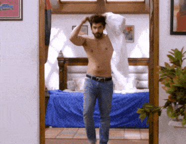 a shirtless man standing in a bedroom with a blue bed