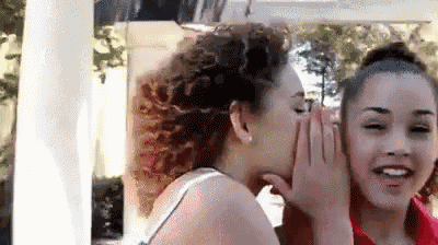 two women are whispering into each other 's ears while standing next to each other .