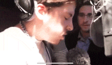 a man wearing headphones is sitting in front of a microphone while another man looks on .