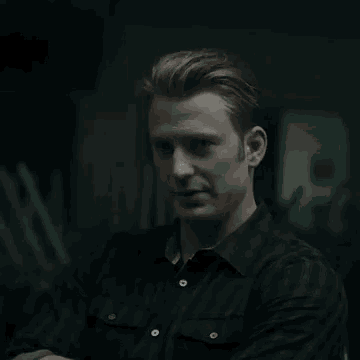 a man in a black shirt is standing in a dark room and looking down .