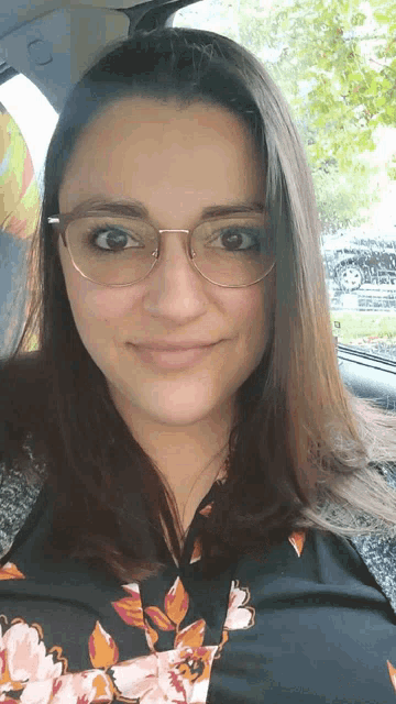 a woman wearing glasses and a floral shirt looks at the camera