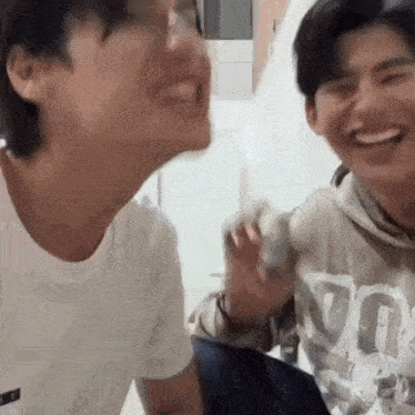 two young men are laughing and looking at each other while sitting next to each other .