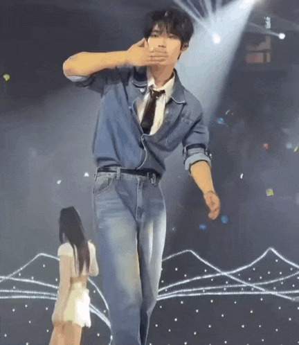 a man in a denim shirt and tie is dancing on a stage with a woman standing behind him