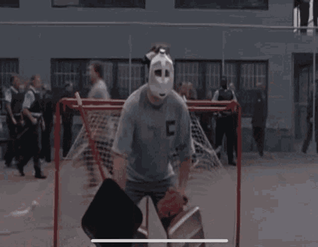 a man wearing a hockey mask is standing in front of a goalie net .