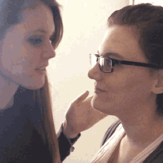 a woman wearing glasses touches the face of another woman