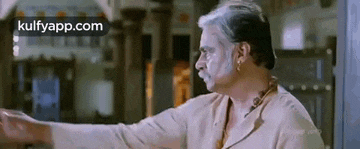 a man with a mustache is standing in a room with his arms outstretched and talking to someone .