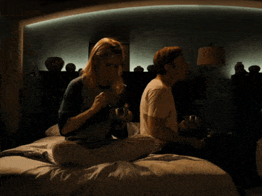 a man and a woman are sitting on a bed and the woman is wearing a shirt that says ny