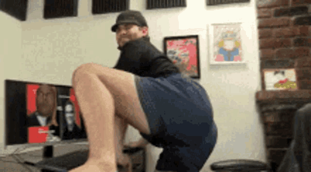 a man squatting on a desk in front of a computer monitor