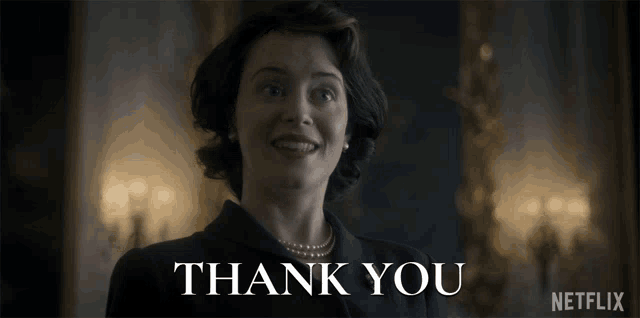 a woman in a suit and pearls is smiling in front of a sign that says " thank you "