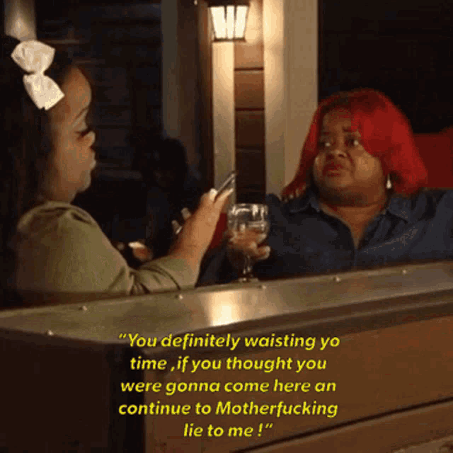 a woman with red hair is talking to another woman while holding a glass of wine