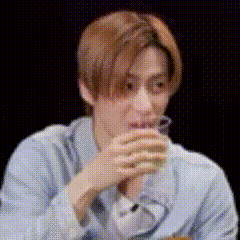 a man in a blue shirt is drinking from a glass while sitting at a table .