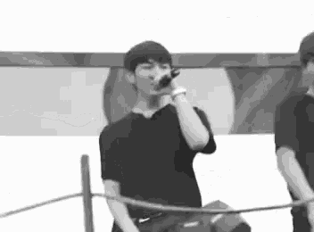 a man is singing into a microphone while standing next to another man in a black and white photo .