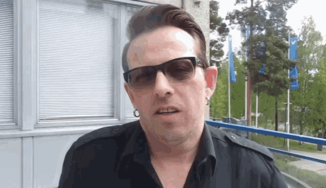a man wearing sunglasses and a black shirt stands in front of a window