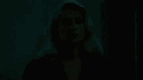 a woman with blonde hair and a black dress is standing in a room .