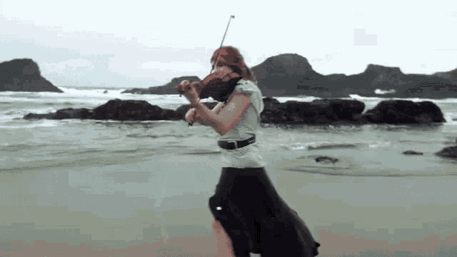 a woman playing a violin on the beach near the ocean