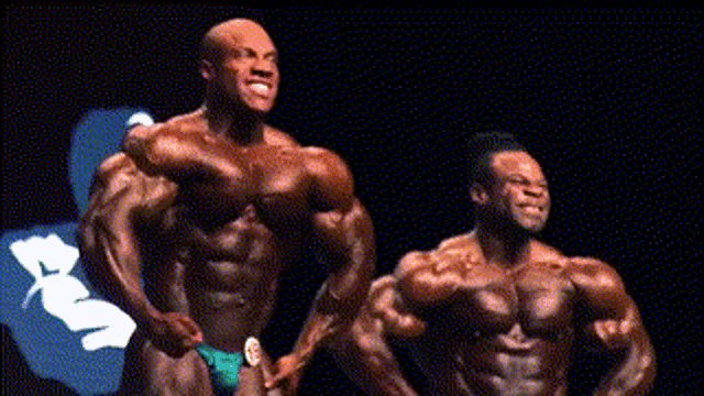 two bodybuilders are posing for a picture and one has a badge on his chest that says ' mr. olympia '