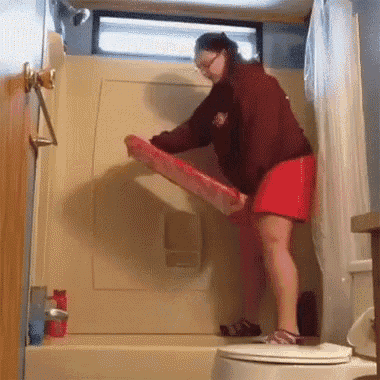 a woman in a red skirt is standing in a shower holding a pink box .
