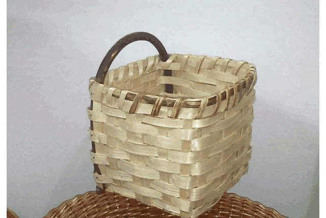 a small basket with a wooden handle is sitting on a wicker basket