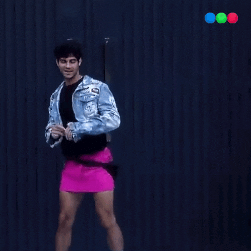 a man in a denim jacket and pink skirt is dancing with the word iconic behind him