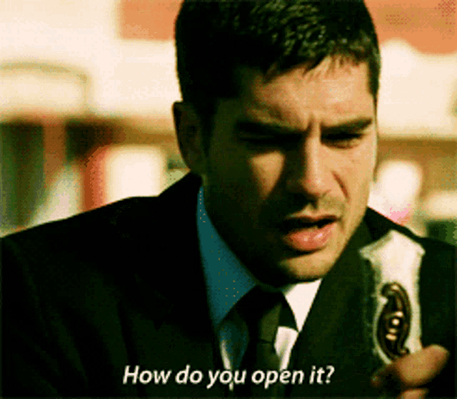 a man in a suit and tie is holding a bottle and asking how do you open it
