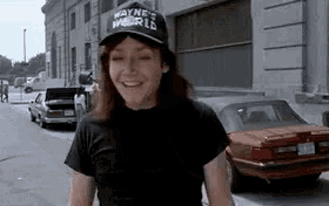 a woman wearing a wayne 's world hat is smiling while standing on a sidewalk .