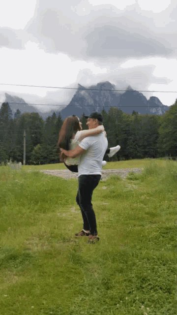 a man is carrying a woman in his arms in a field with mountains in the background