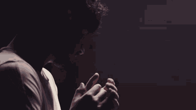 a man in a white t-shirt is holding his hand out in the dark .